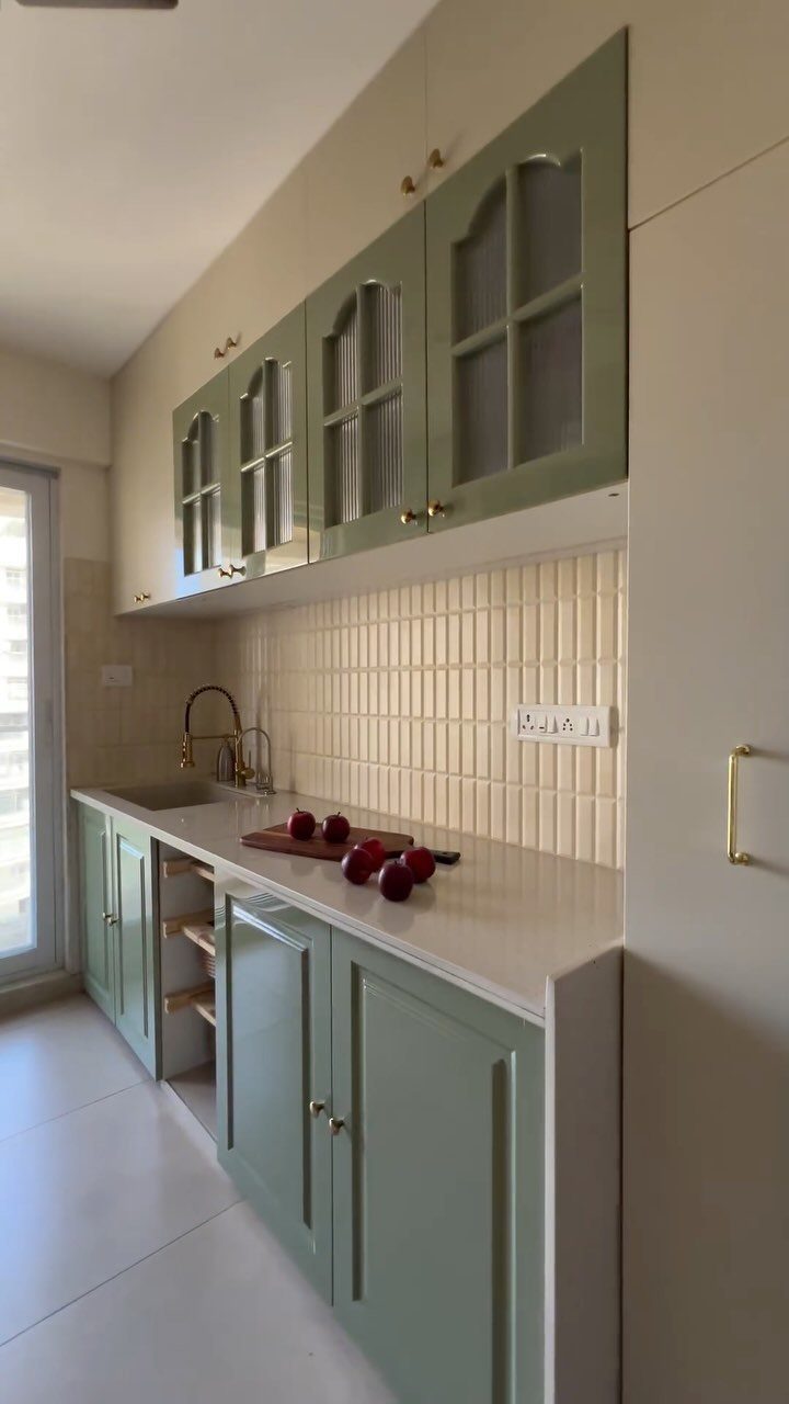 Sage green kitchenette with white countertops, tiled backsplash, and gold hardware.