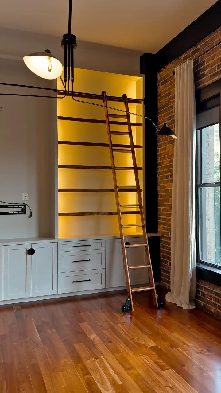 Wooden rolling ladder leaning against yellow backlit shelves above white storage cabinets.