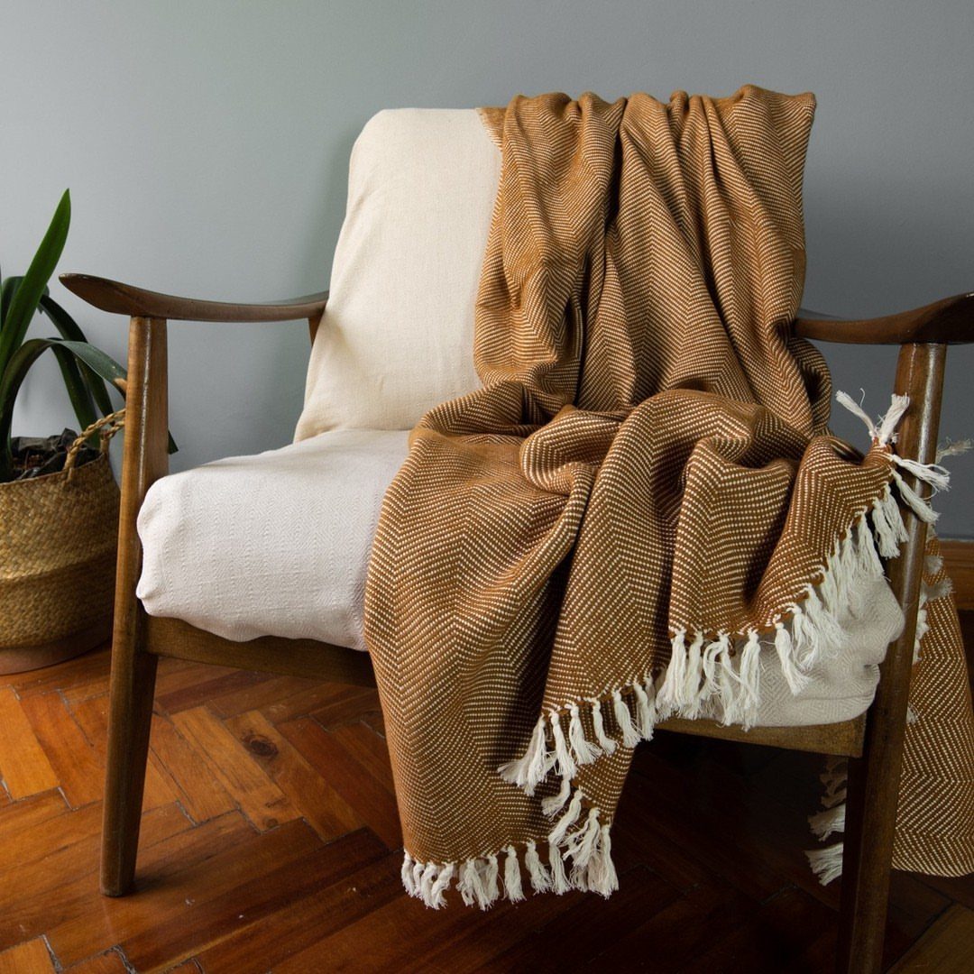 Brown herringbone throw blanket draped over a white cushioned wooden armchair.