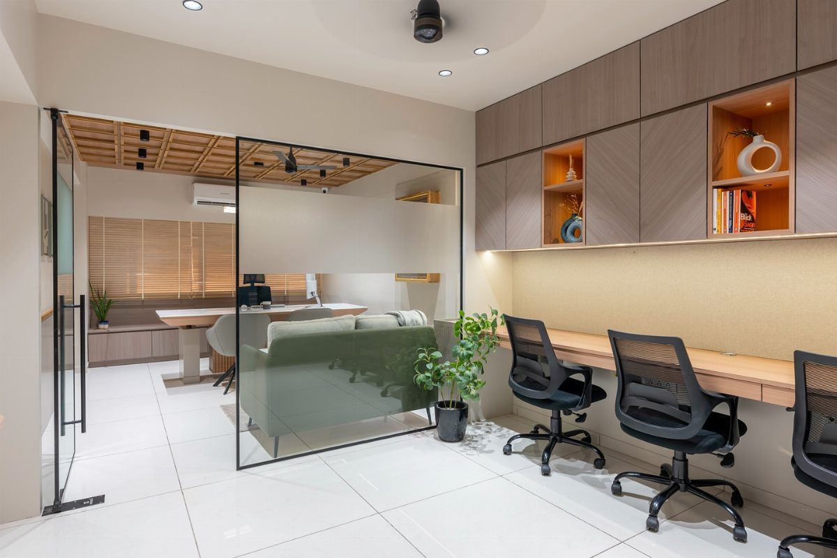 Modern office interior with a long wooden desk, black chairs, and glass partition.