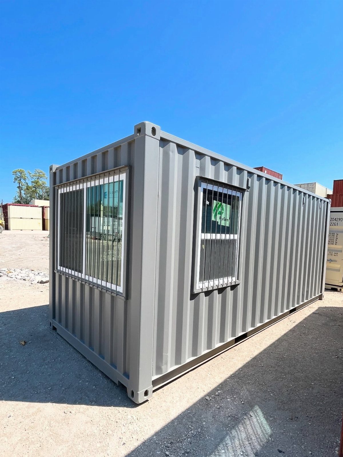 Grey shipping container office with two windows on a sandy lot.
