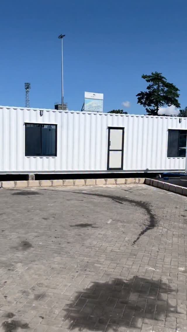 White shipping container office with windows and door on a paved lot.