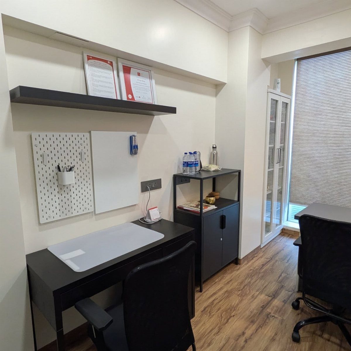 Small office with black desk, chair, and shelving against white walls and wood floors.