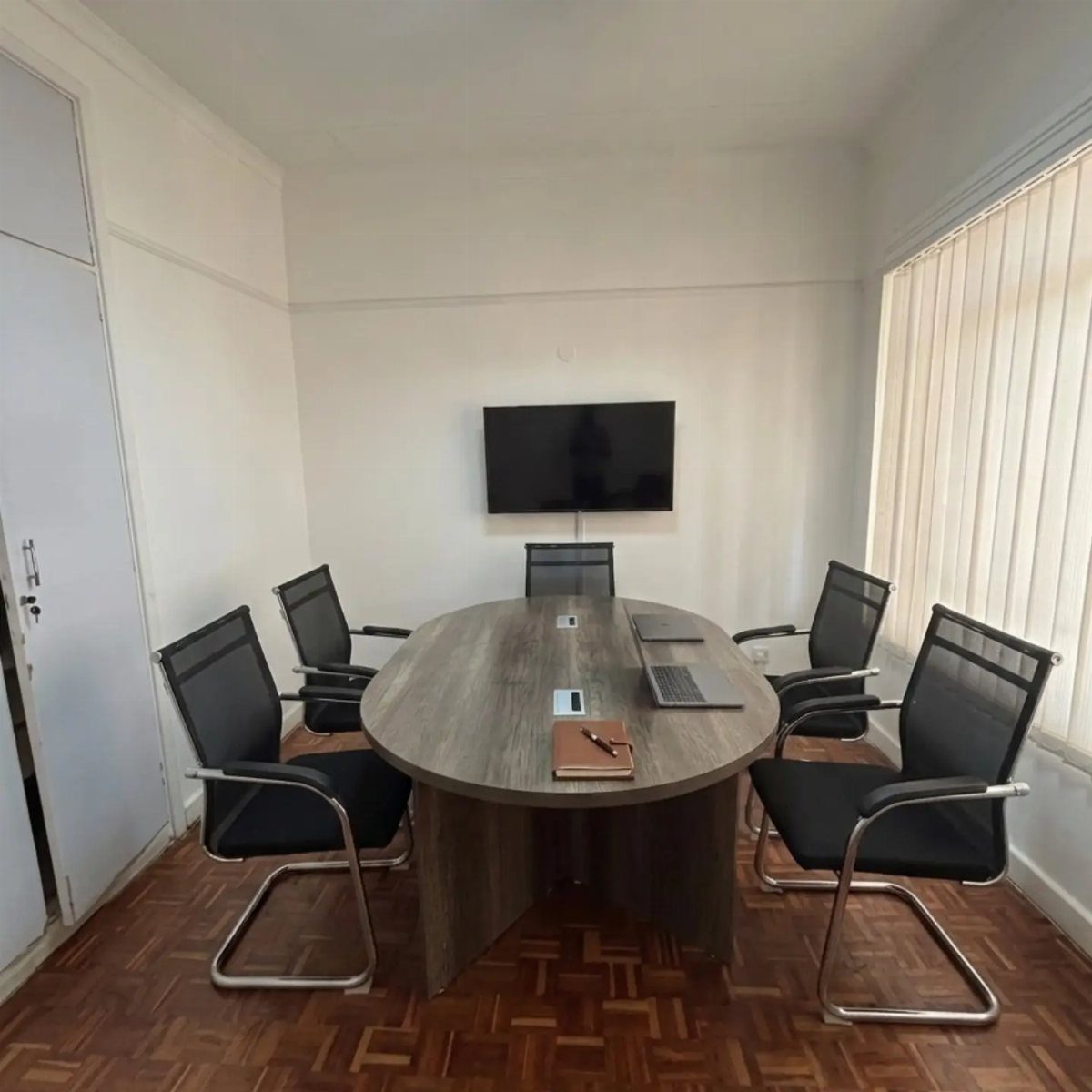 Oval wooden conference table with black mesh chairs in a small white office.
