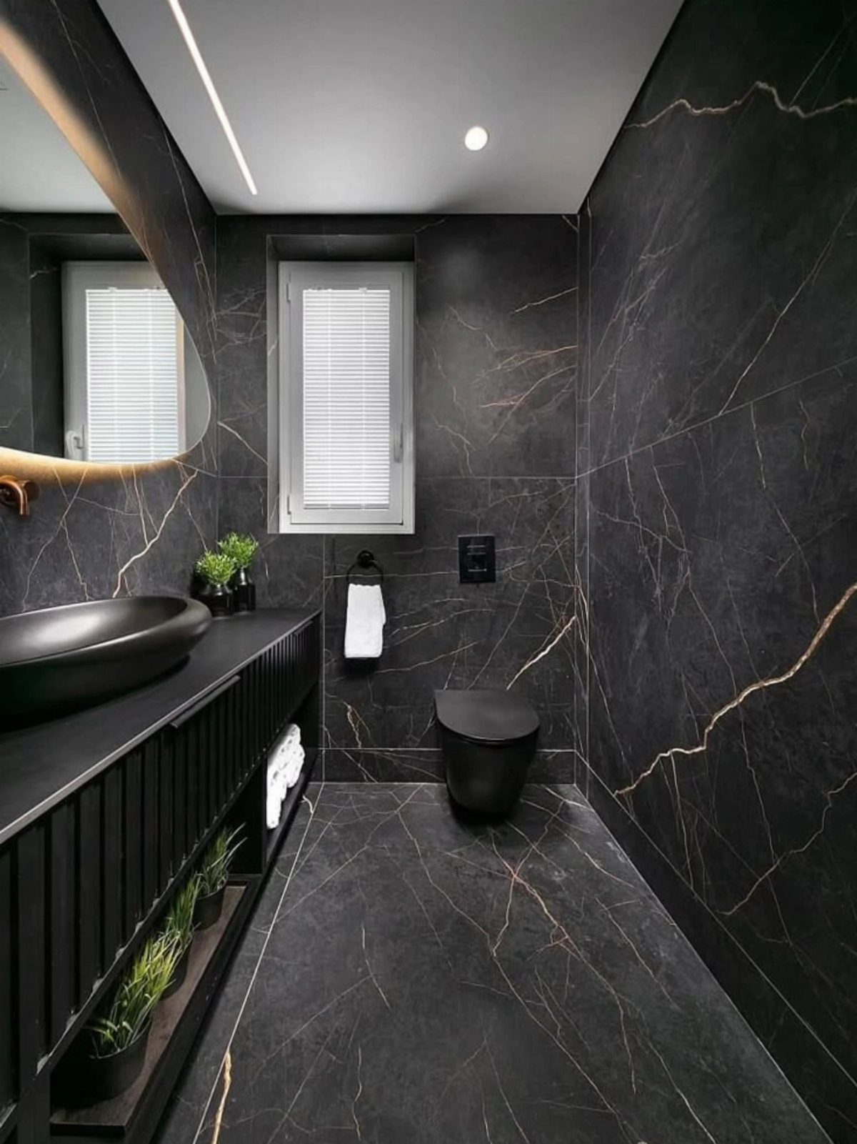 Modern black marble bathroom with gold veining, black sink, and black toilet.