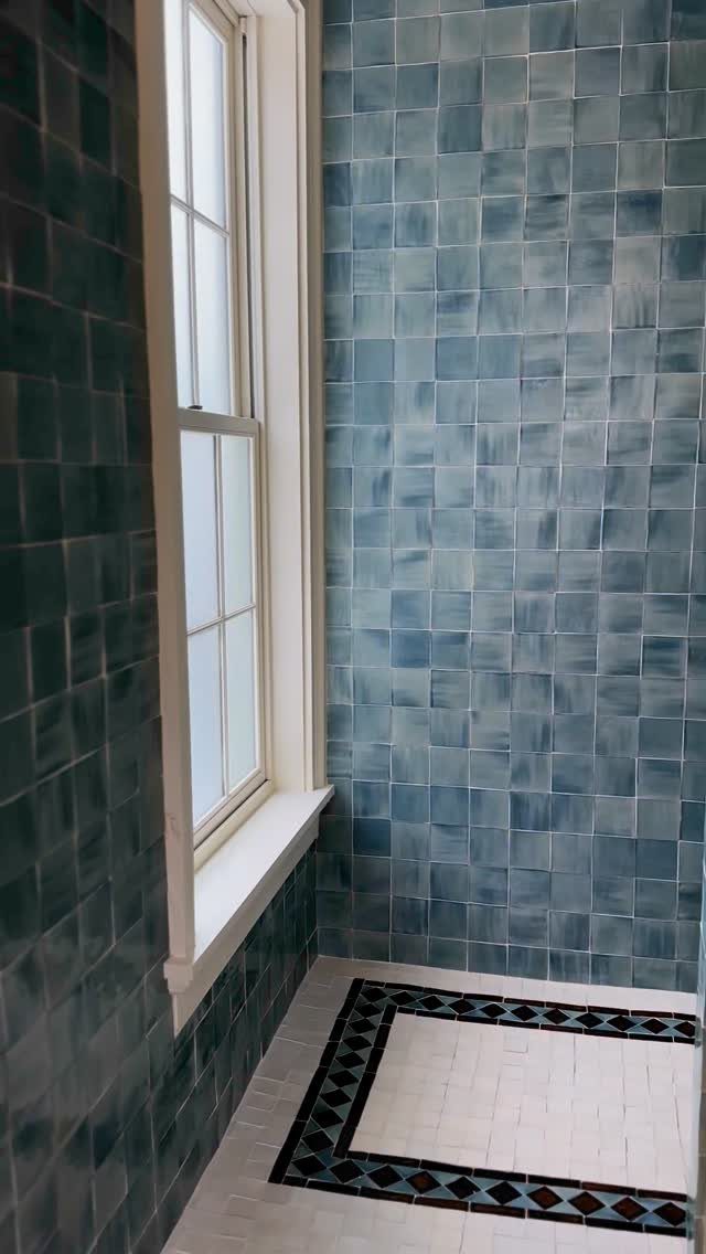 Blue-grey square wall tiles and a decorative bordered floor in a bathroom.