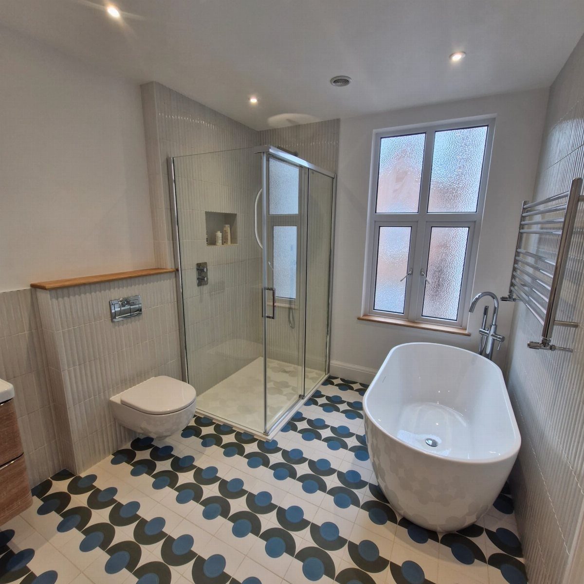 Modern bathroom with bold blue patterned floor tiles, freestanding tub, and glass shower.