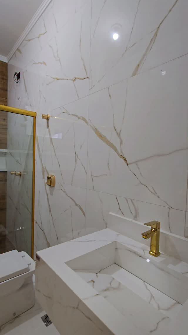 Small bathroom with white and gold marble tiles, gold faucet, and glass shower.