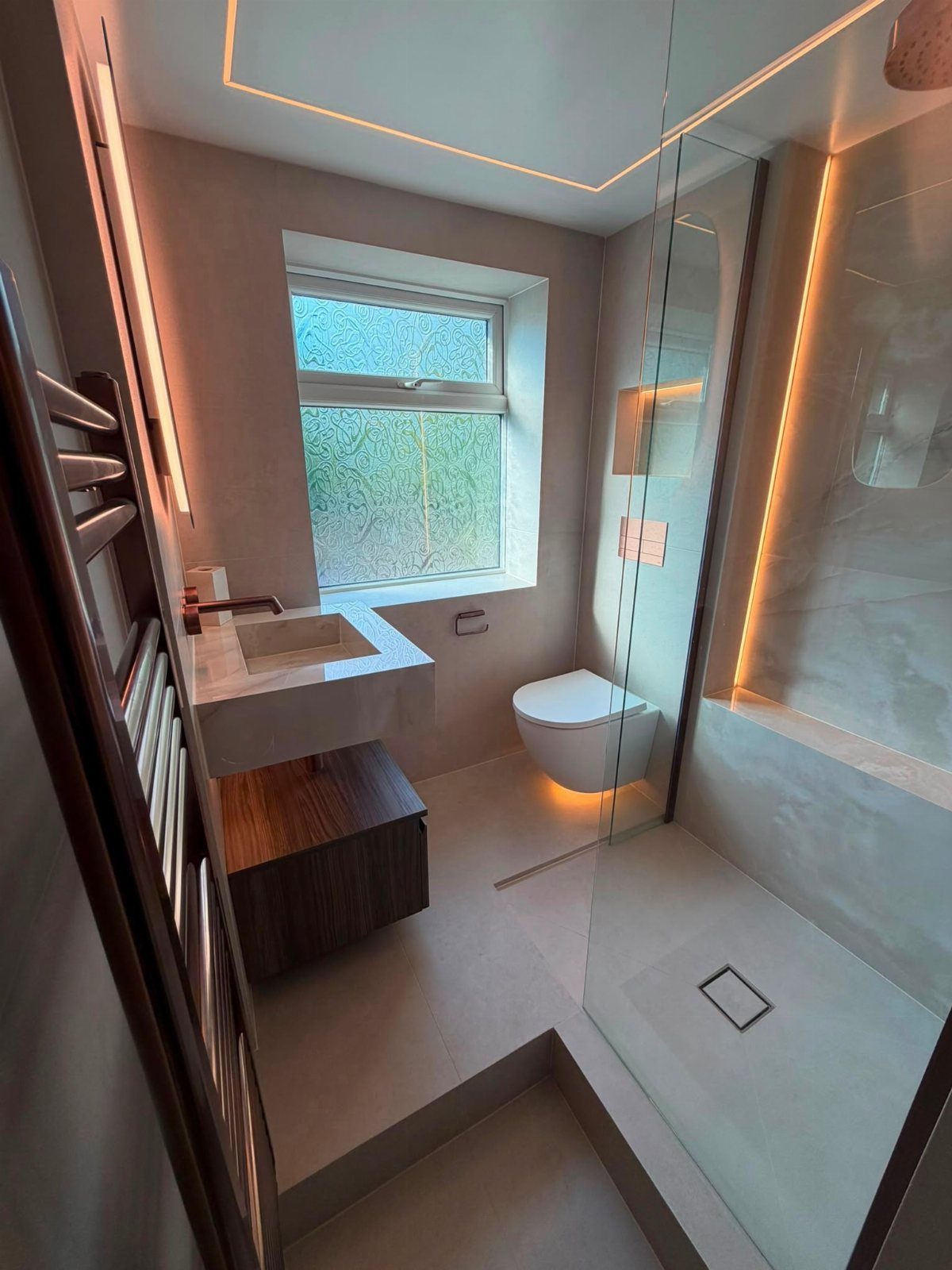 Modern small bathroom with seamless grey microcement surfaces and warm integrated LED lighting.