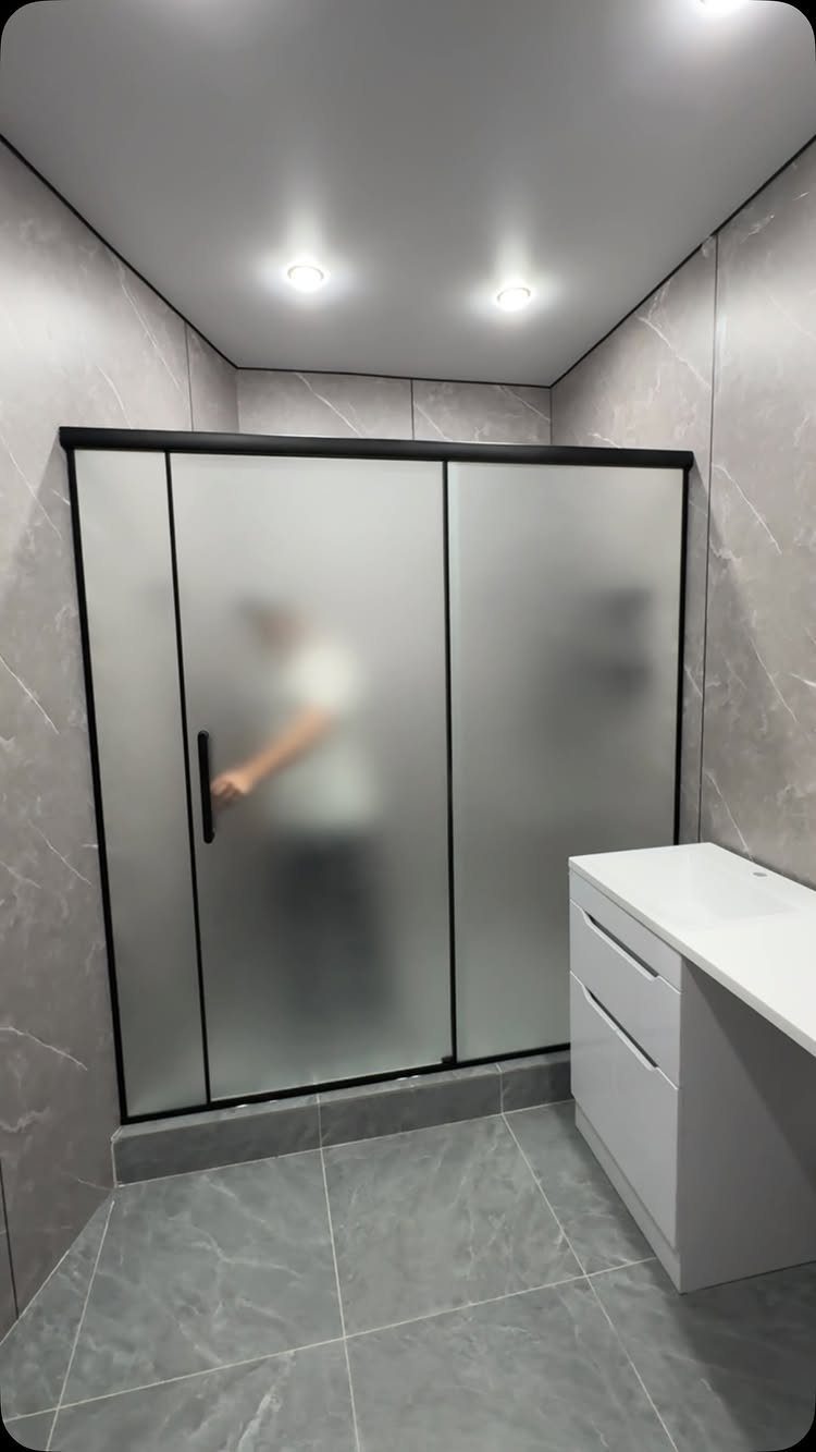 Frosted glass sliding shower doors with black frames in a grey marble bathroom.