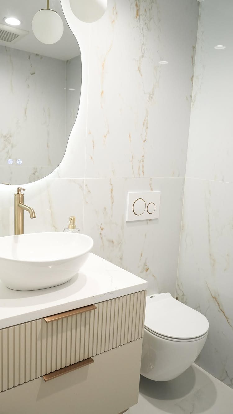 Small bathroom with white marble tiles, a vessel sink, and a large curved mirror.
