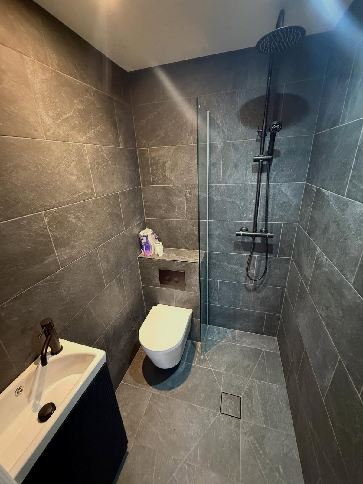 Dark grey tiled bathroom featuring a wet room design with a walk-in shower.