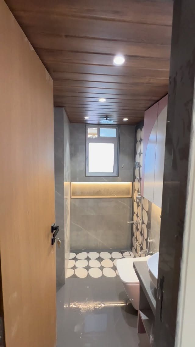 Narrow bathroom with grey tiles, wooden ceiling, and white circular wall accents.
