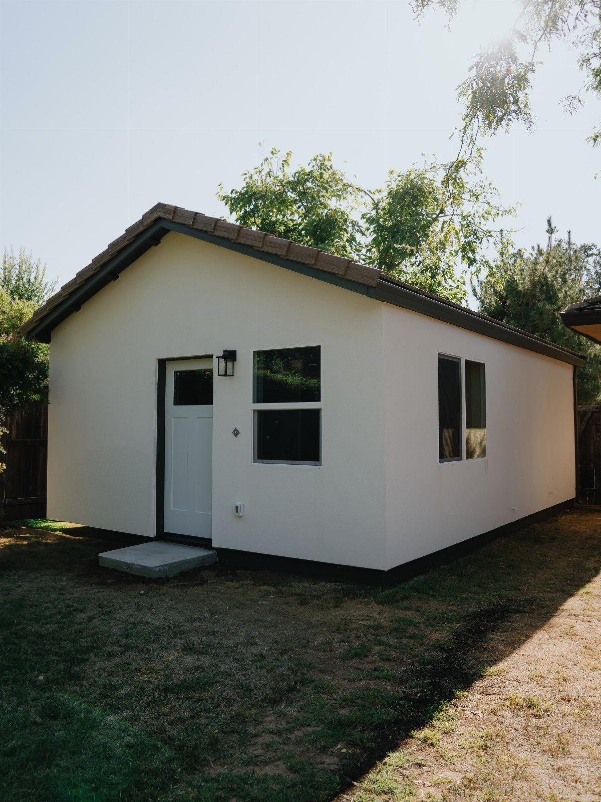 Small white accessory dwelling unit with a brown roof on a grassy lawn