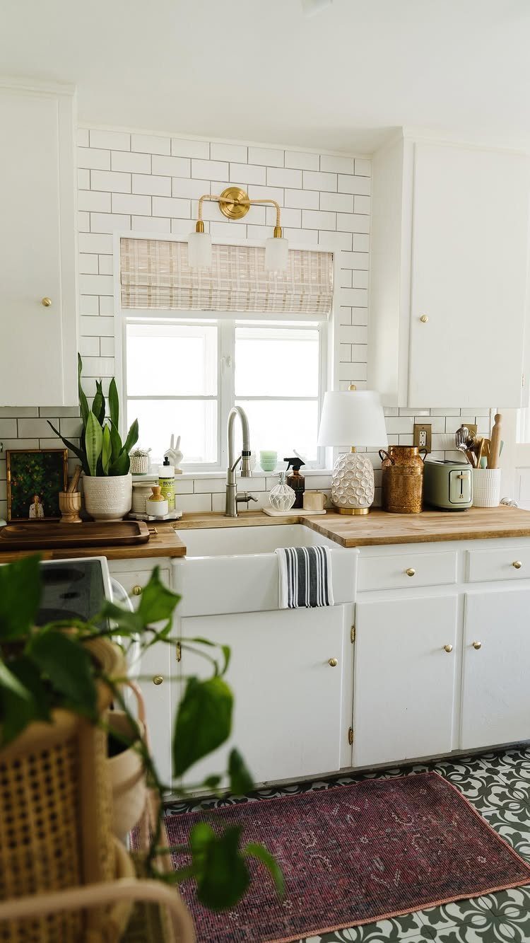 White kitchen with wooden countertops, farmhouse sink, and a red patterned floor rug.