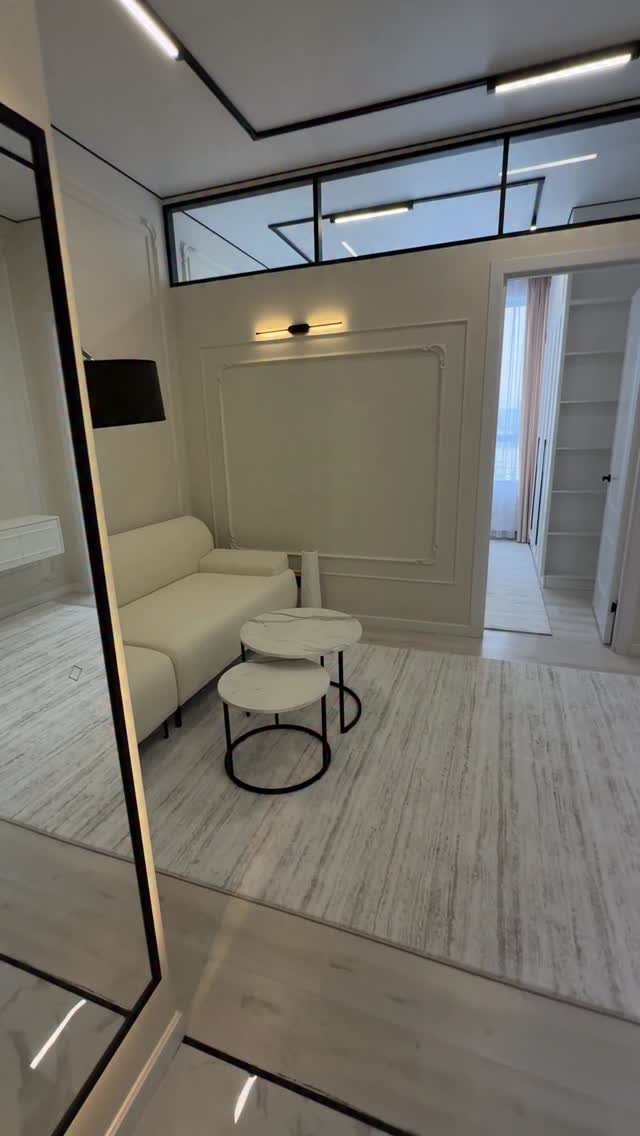 Modern minimalist living room with white sofa, round tables, and linear ceiling lighting.