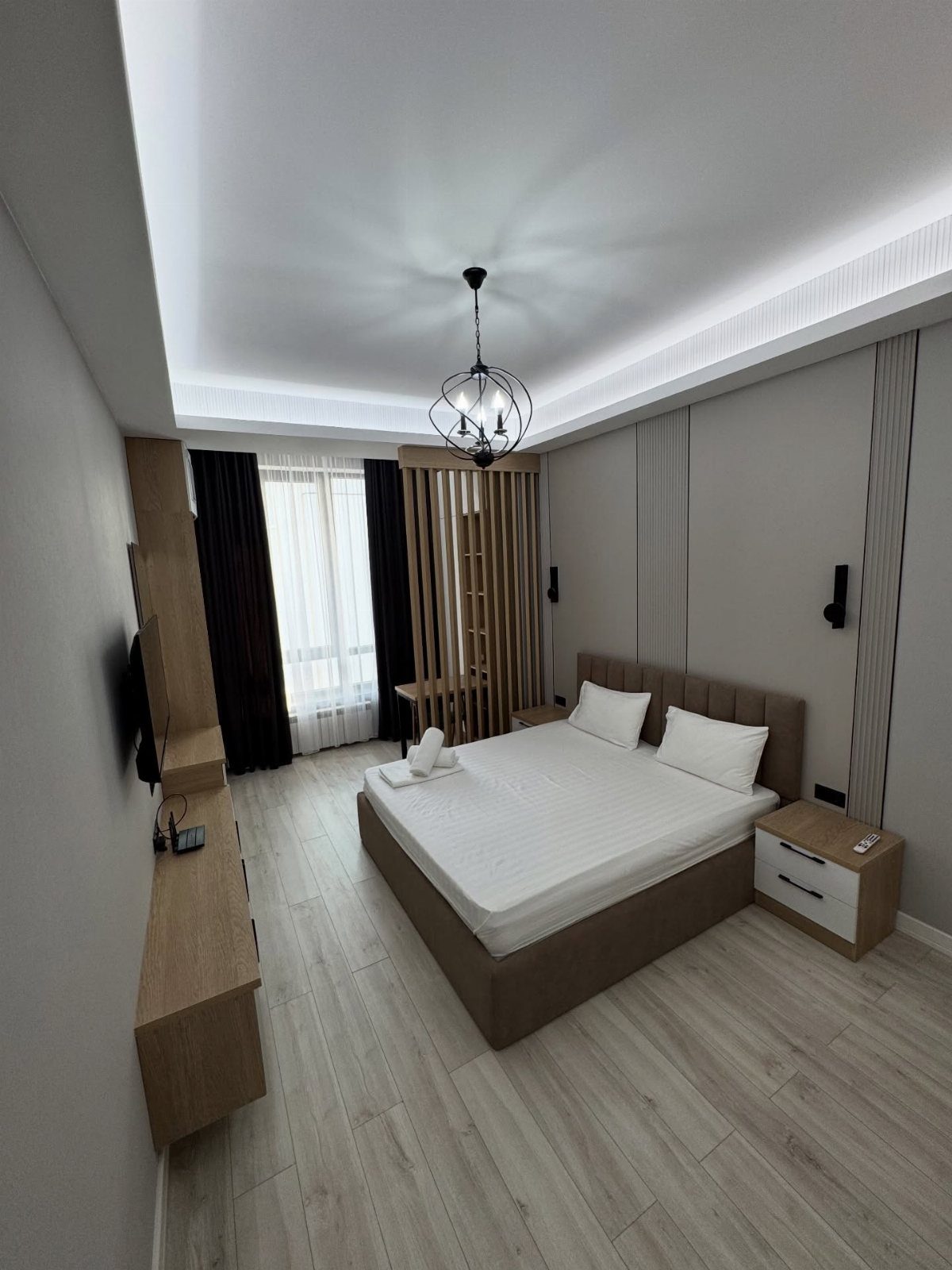 Modern bedroom with a large bed, light wood floors, and a slat divider.