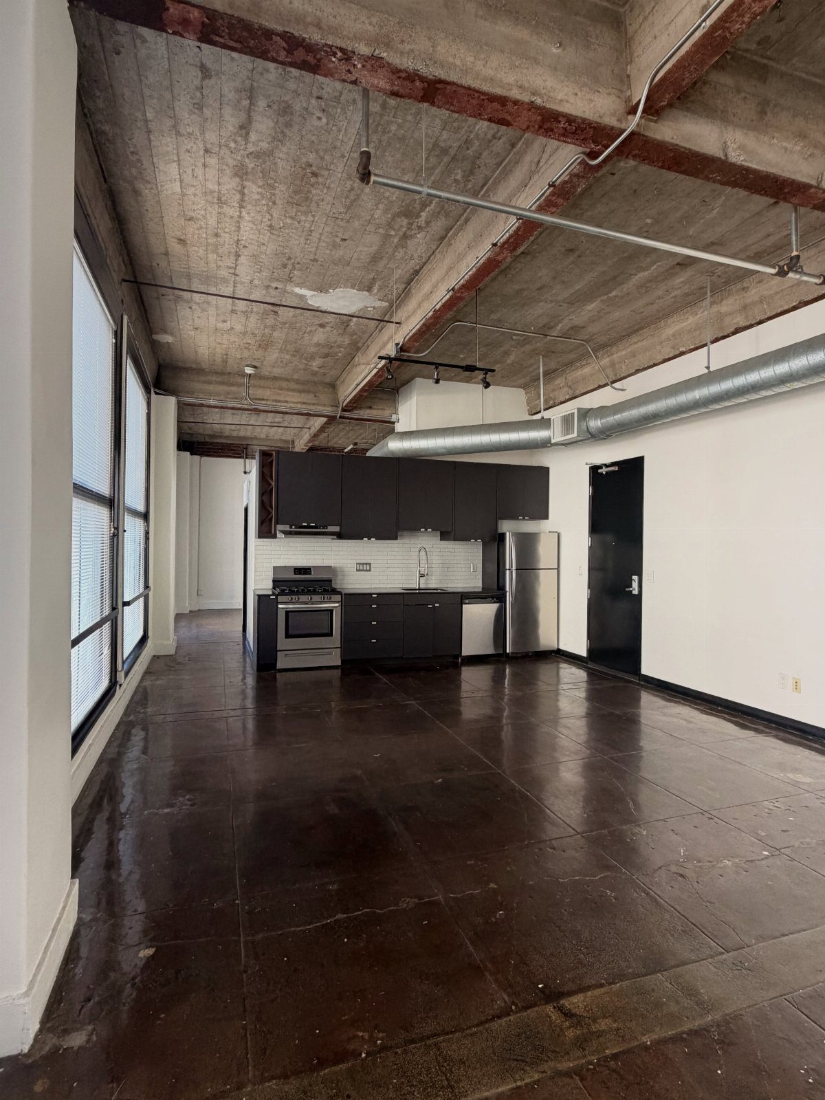 Industrial loft apartment with polished concrete floors and a small dark kitchen area.