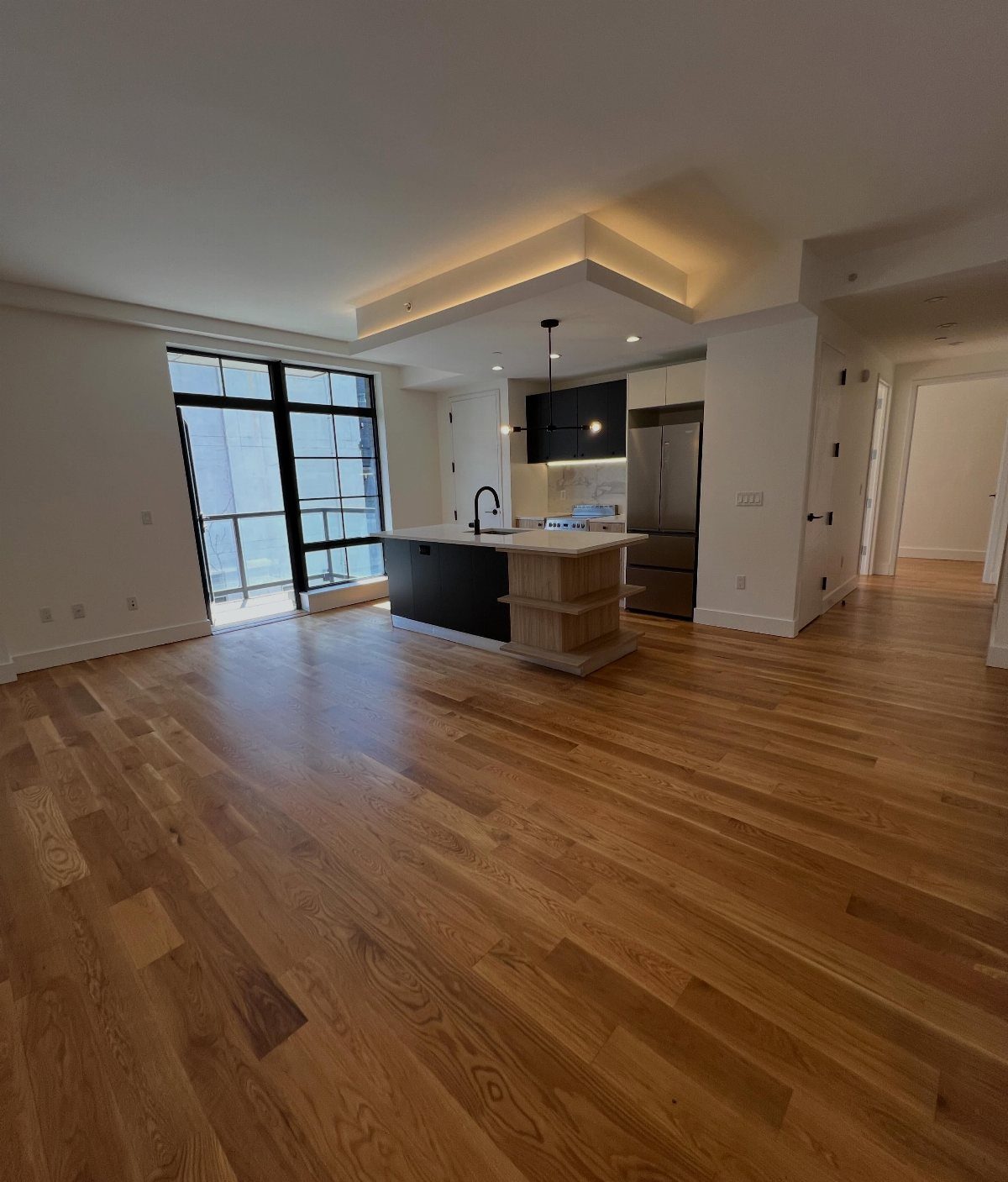 Empty modern apartment interior with hardwood floors and a contemporary kitchen area.