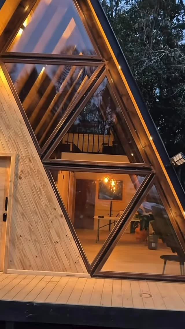 A-frame cabin with large geometric windows showing a warm interior loft and living area.