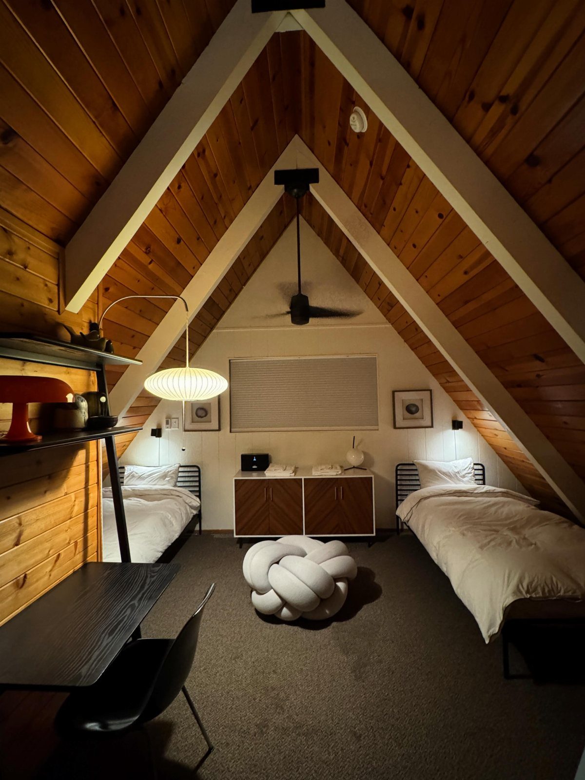 Bedroom in an A-frame cabin with slanted wood ceilings and two single beds.