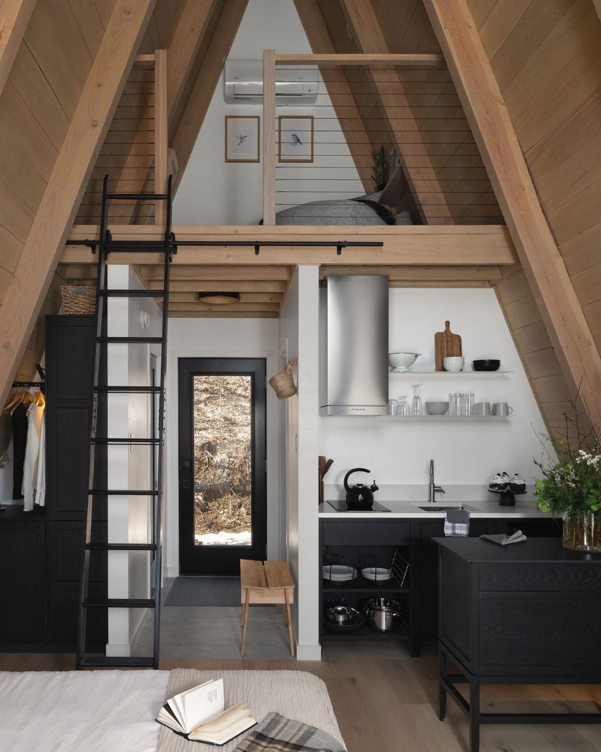 Wooden loft safety railing in an A-frame cabin above a modern black kitchen.
