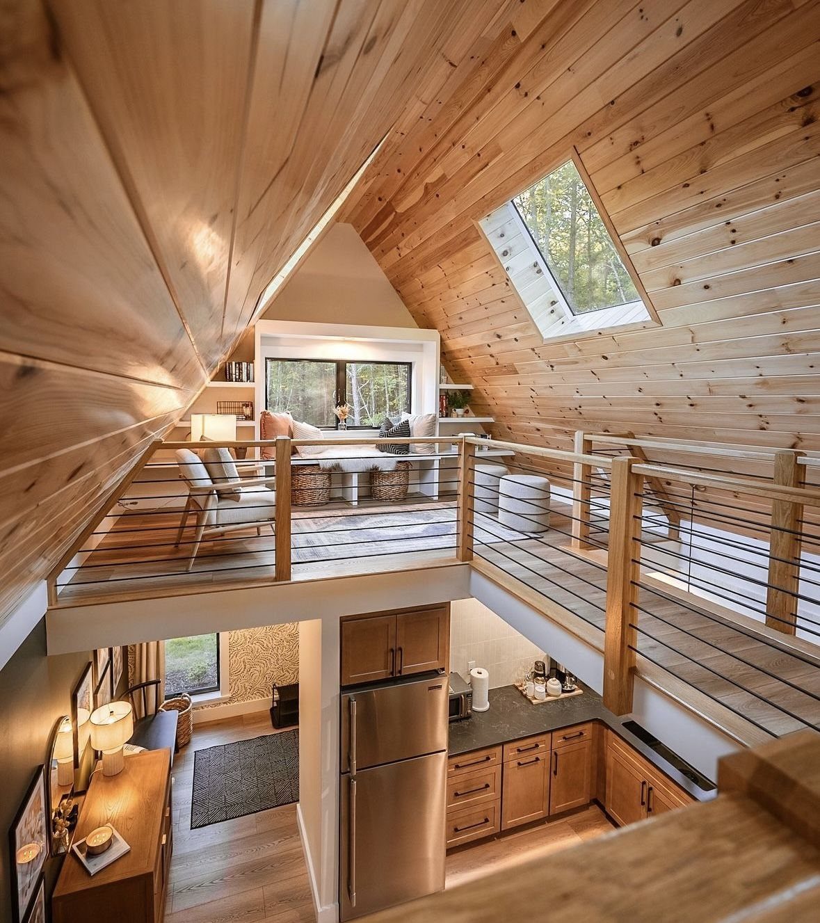 A-frame cabin interior showing a loft overlooking an open-concept kitchen and living area.