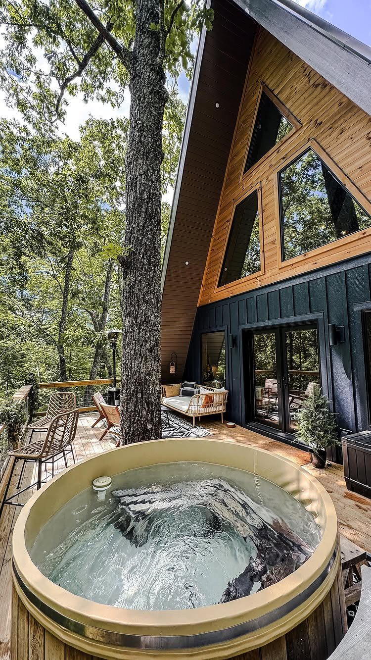 Wooden deck with a round hot tub outside a modern A-frame cabin.