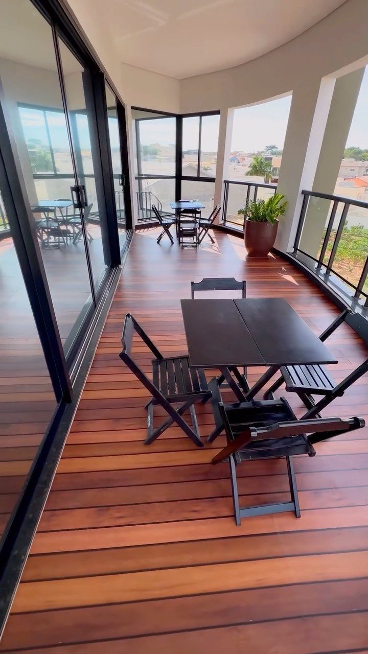 Modern balcony with wood flooring, black folding furniture, and a potted plant.