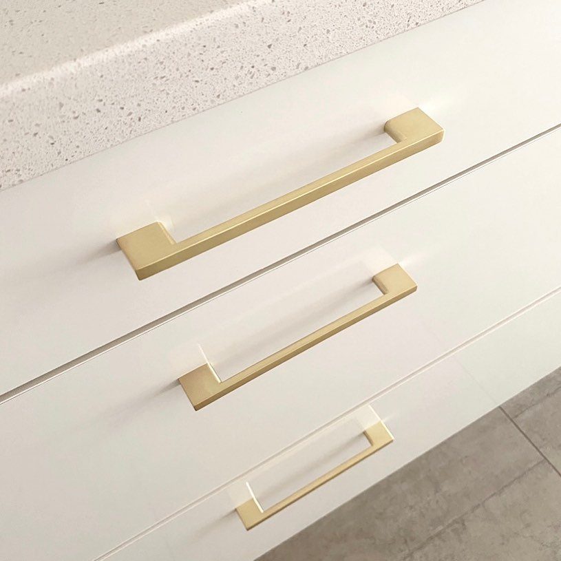 Gold metal bar handles on white drawers beneath a speckled white countertop