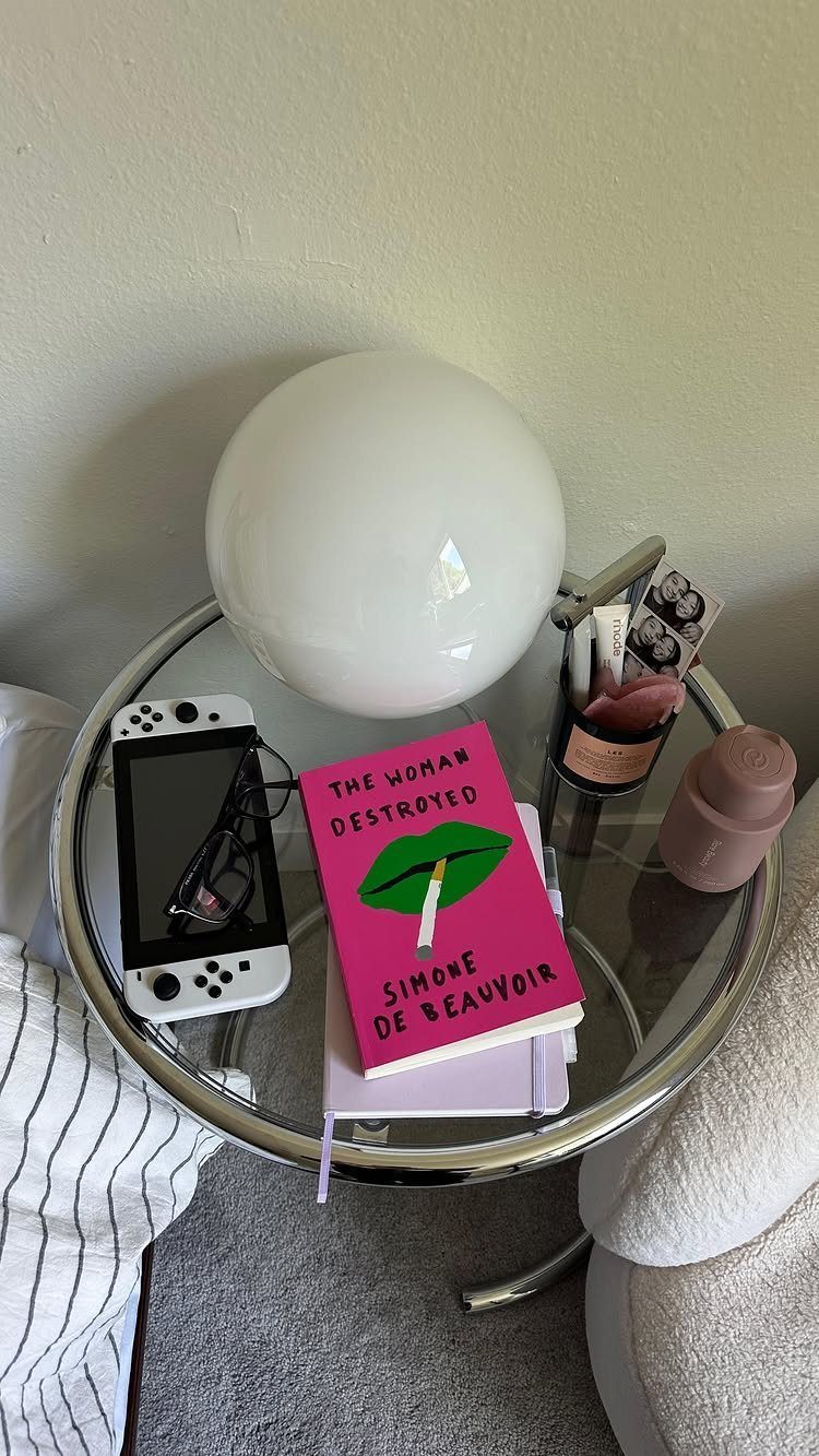 Round glass side table with a globe lamp, pink book, and gaming console.