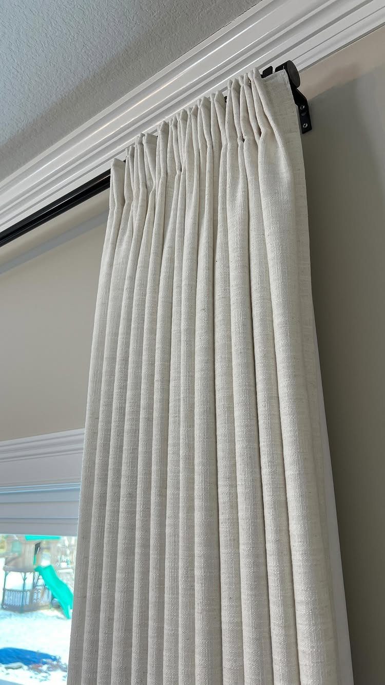 Cream linen curtains hanging from a black rod near the ceiling crown molding.