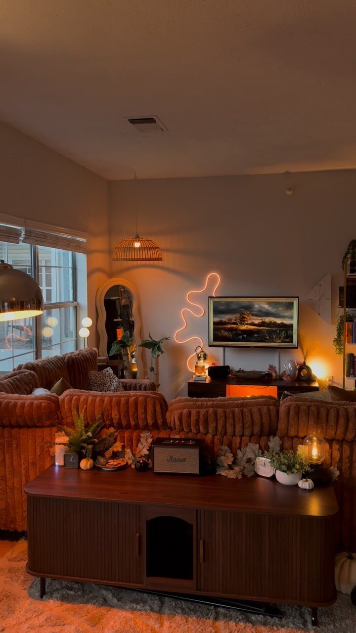 Cozy living room with brown corduroy sofa, wooden sideboard, and warm neon lighting.