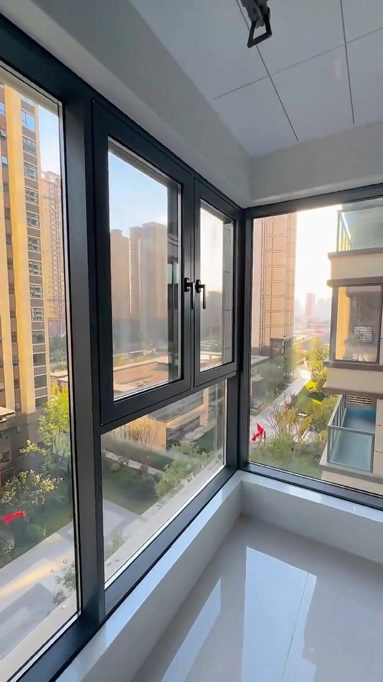 Large black-framed windows in a bright room overlooking a city skyline and trees.