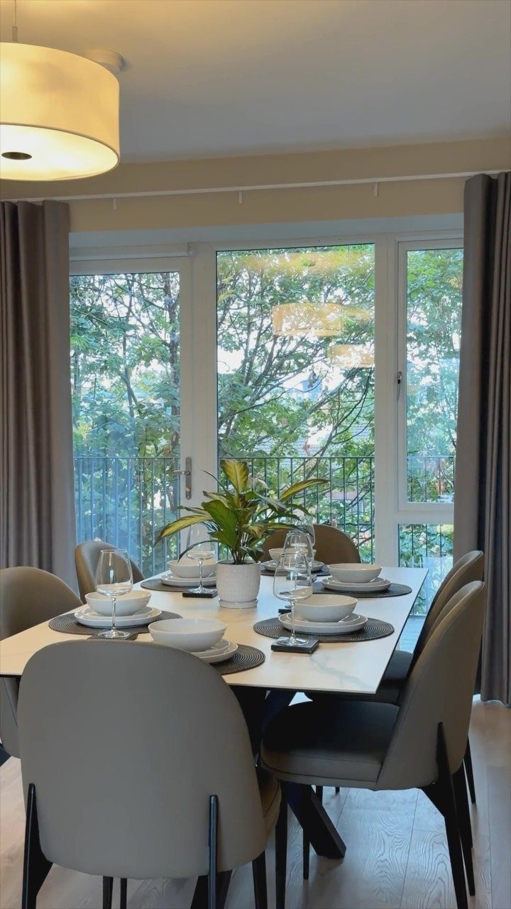 Dining room with a set table and large windows overlooking green trees.