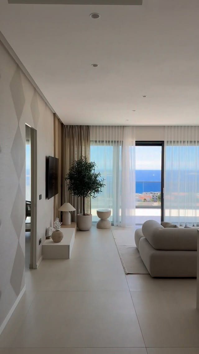 Modern apartment living room with large floor-to-ceiling windows overlooking the blue ocean.