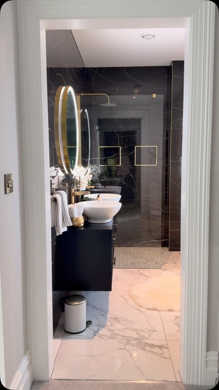 Black marble bathroom with a black vanity, white vessel sink, and gold fixtures.