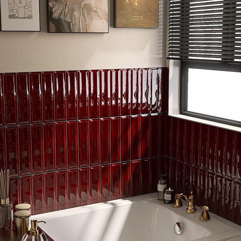 Bright red glossy wall tiles in a bathroom with a white bathtub and gold fixtures.