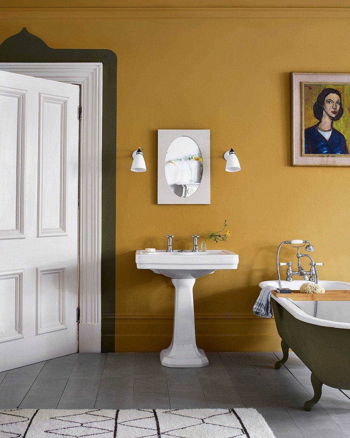Mustard yellow bathroom walls with a white pedestal sink and green clawfoot tub.