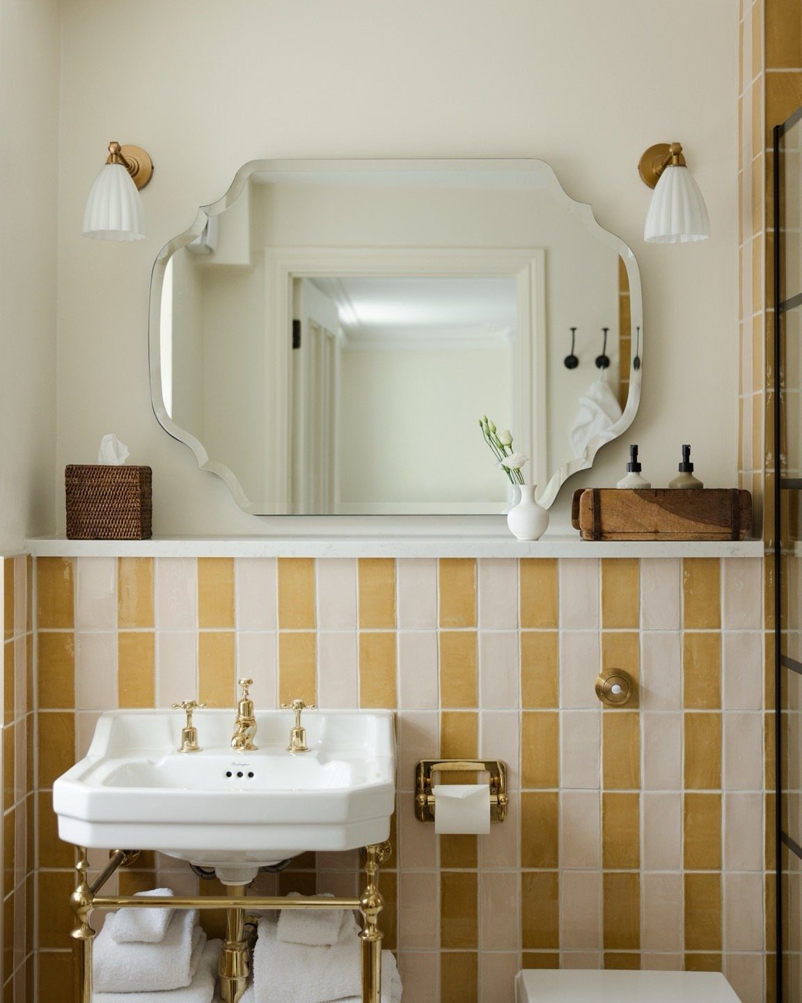 Bathroom with soft yellow and cream striped tiles, white sink, and gold fixtures.