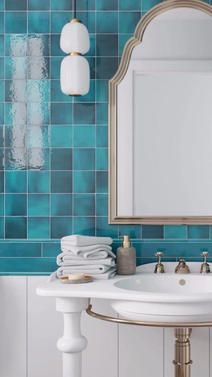 Teal tiled bathroom wall with a white pedestal sink and gold mirror frame.