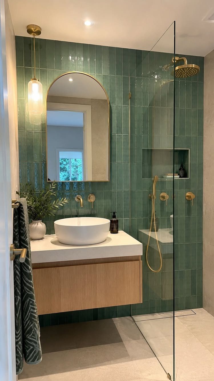 Teal-green vertical wall tiles in a modern bathroom with gold fixtures and wood vanity.