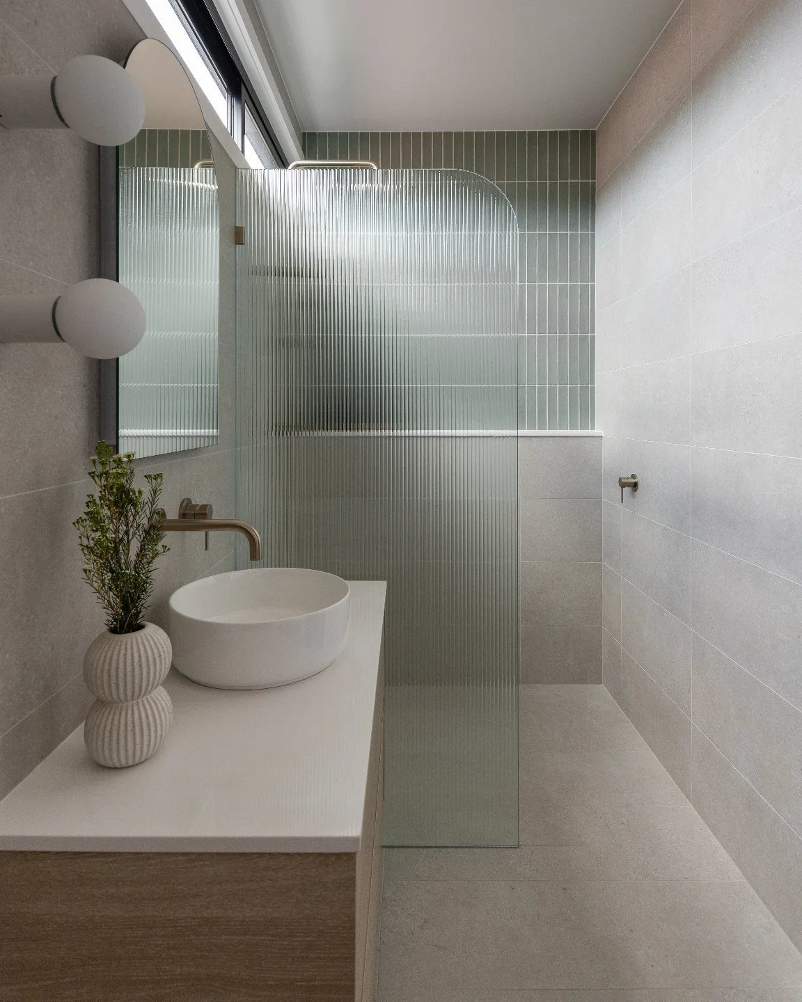 Curved glass shower panel in a modern bathroom with white vessel sink and grey tiles
