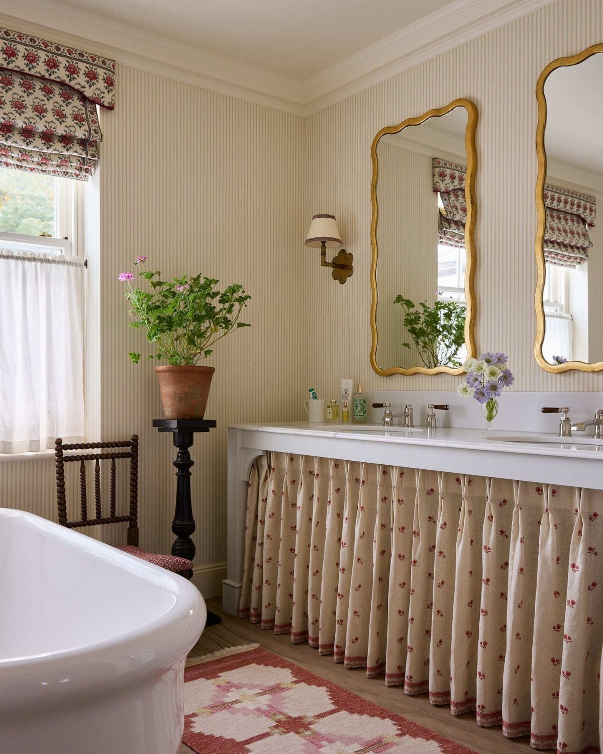 Traditional bathroom with a floral vanity skirt, patterned rug, and gold-framed mirrors.