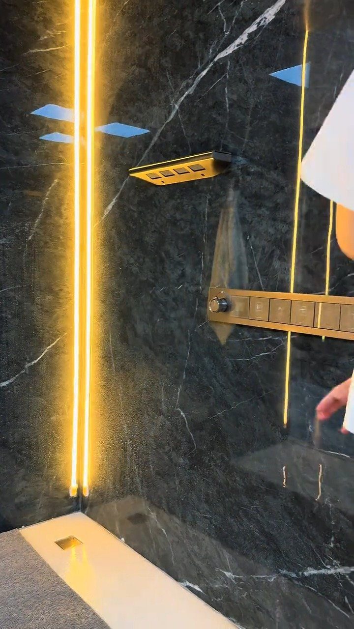 Dark marble shower walls with vertical gold light strips and gold fixtures.