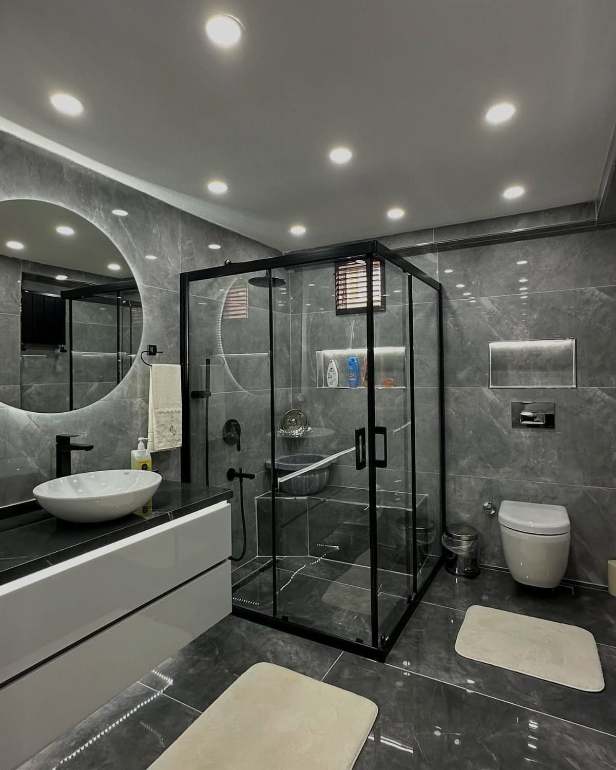 Large circular backlit mirror above a white floating vanity in a grey marble bathroom.