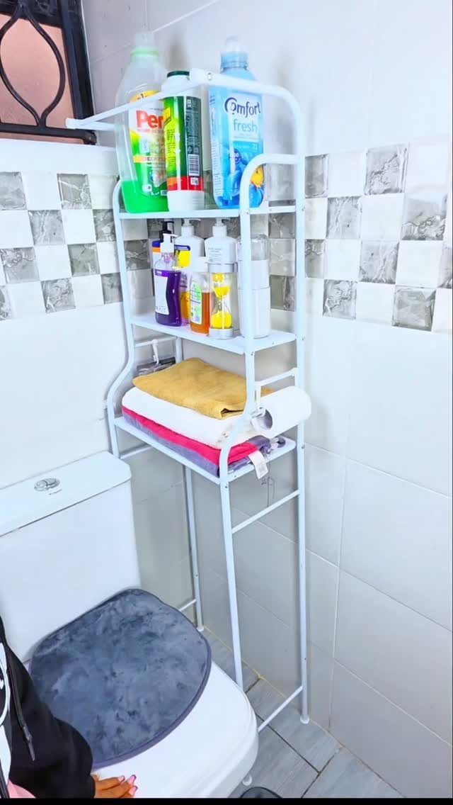 White metal shelving unit over a toilet holding cleaning supplies and towels.