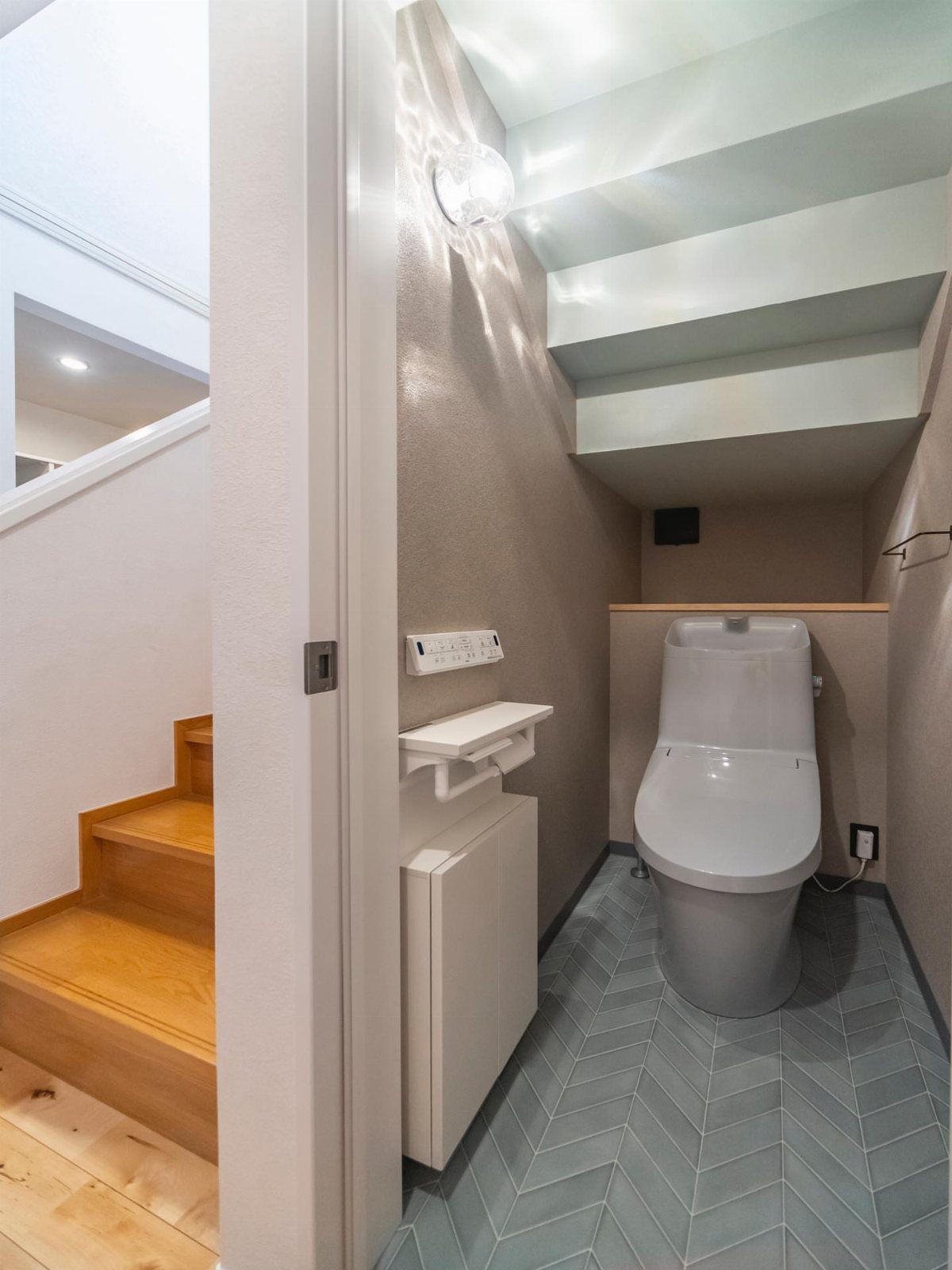 Small bathroom under a staircase with a white toilet and grey herringbone tiles.