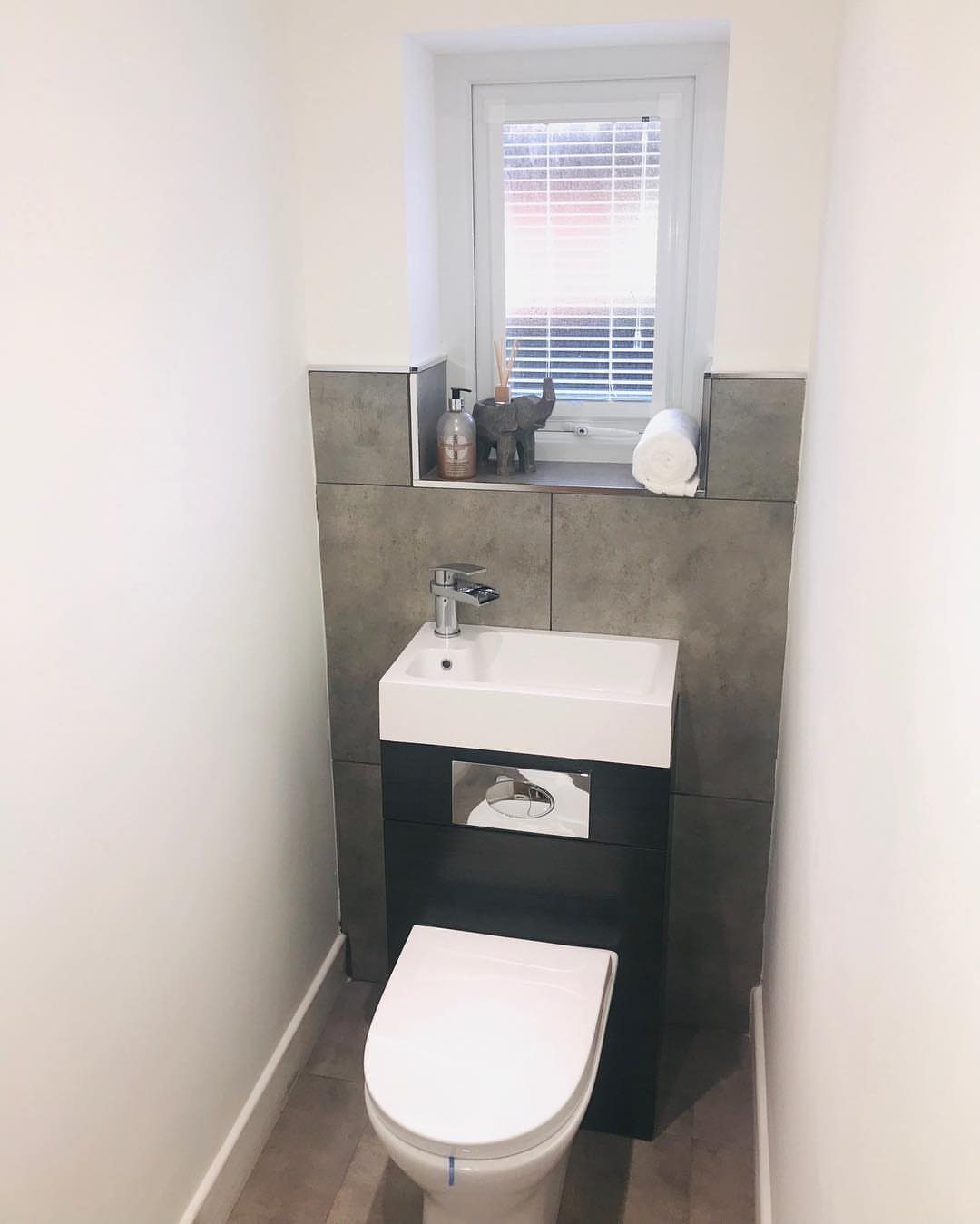 Compact white sink and toilet in a small bathroom with grey tiles.