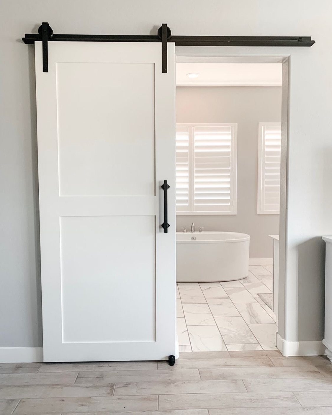 White sliding barn door opening into a bright bathroom with a freestanding tub.